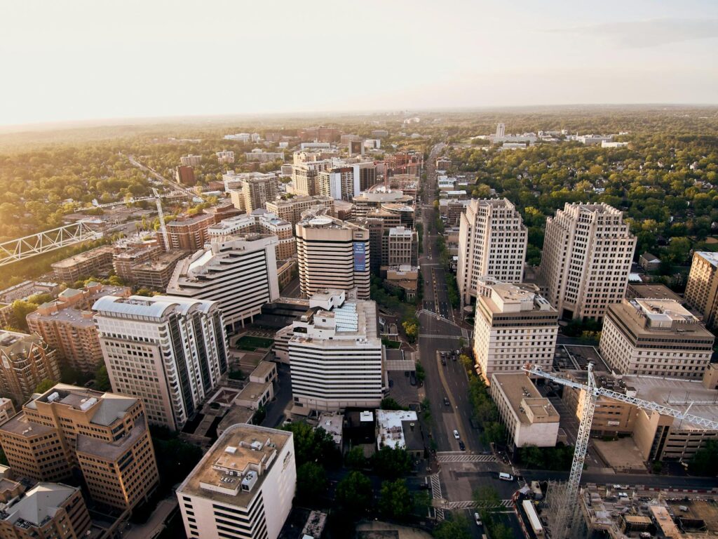 Aerial view of a modern city skyline with construction and greenery at sunset.